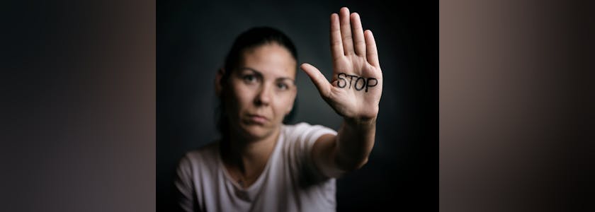 Photo d'une femme qui brandit sa main sur laquelle est écrit STOP, illustrant le harcèlement, la violence