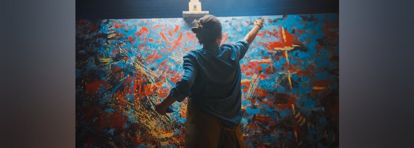 Talented Female Artist Works on Abstract Oil Painting, Using Paint Brush She Creates Modern Masterpiece. Dark and Messy Creative Studio where Large Canvas Stands on Easel Illuminated.