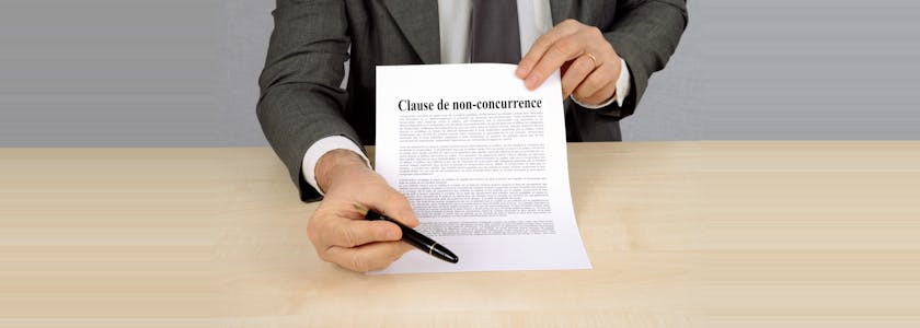 Un homme tient une feuille contenant une clause de non-concurrence dans une main et dans l'autre un stylo pour signature de la clause