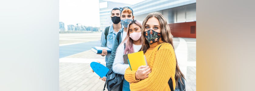 Portrait de quatre étudiants portant des masques devant un bâtiment