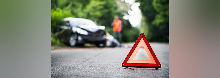 A close up of a red emergency triangle on the road in front of a car after an accident.