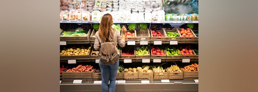 Good looking woman standing in front of vegetable shelves choosi