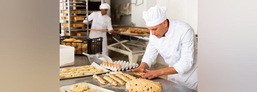 Male baker working with dough forming baguettes