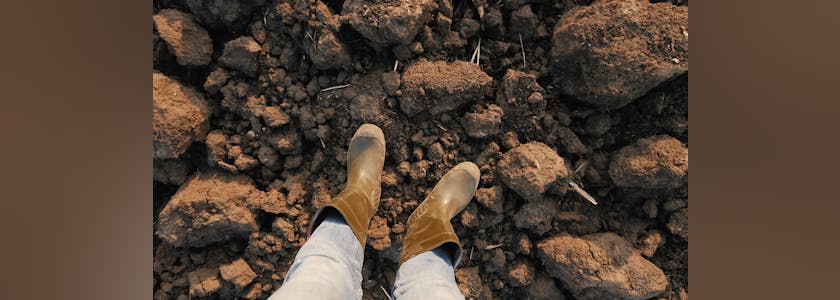 Top view male farmer in rubber boots standing on plowed field