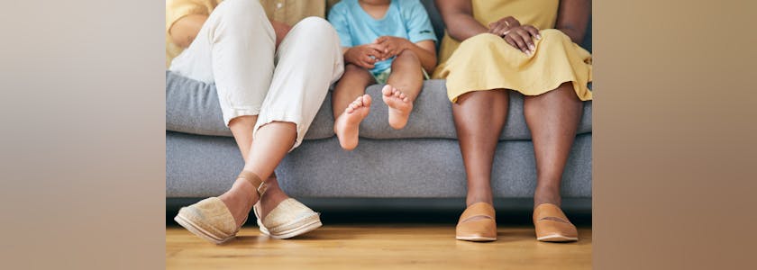 Legs, gay couple and a family on a home sofa for security, quality time and love. Feet of women or lesbian parents and a young child together in a living room with trust, care or support for adoption