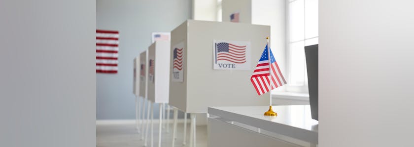 Empty polling station with white voting booths and American flag. Elections in the United States.